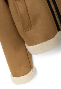 Chaqueta de ante marrón con puños y collar de borrego. Presenta una cremallera negra y un bolsillo lateral. Textura suave en toda la prenda.