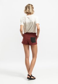 Bordeaux shorts met een zwarte denim zak, omgeslagen uiteinden, gecombineerd met een wit T-shirt met een kleurblokontwerp op de achterkant.