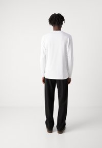 Camisa branca de manga longa com decote redondo, combinada com calças largas pretas. Tecido suave e corte descontraído, adequado para uso casual.