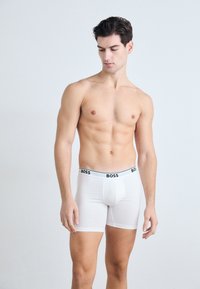 Weiße Baumwoll-Boxershorts mit einem schwarzen "BOSS"-Bund. Der Stoff ist glatt und das Design hat eine taillierte Form.