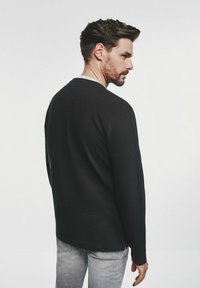 Czarna koszula z długim rękawem o żebrowanej fakturze i okrągłym dekolcie, widok z tyłu. Uzupełniona jasnoszarymi dżinsami.