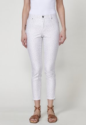Jean skinny à imprimé léopard blanc avec un tissu lisse, deux poches avant et des zips aux chevilles. Associé à des sandales à lanières marron.