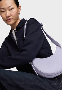 Borsa a spalla in pelle color viola chiaro con logo "TOUS" in rilievo, finita con una superficie testurizzata e una sottile tracolla regolabile.