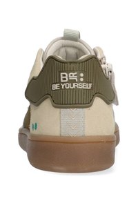 Beige und olivgrüne Sneaker mit einer strukturierten Rückseite, die "BE YOURSELF" geprägt hat, und einer braunen Gummisohle mit Chevron-Muster.