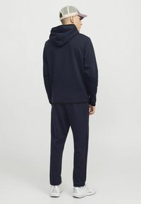 Marineblaue Kapuzenjacke mit Kordelzug, kombiniert mit passenden Jogginghosen. Sie hat ein schlichtes Design und gerippte Bündchen und wird mit weißen Sneakers getragen.