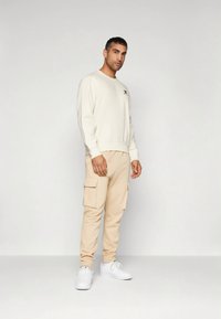 Kremfarvet sweatshirt med rund halsudskæring, beige cargobukser med sidelommer og hvide sneakers. Simpelt design og blød tekstur.