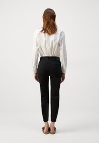 Svarta högmidjade skinny jeans med en åtsittande siluett. Slät denimtyg, bakfickor, ihopparat med en vit skjorta.