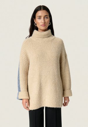 Beige übergroßer gestrickter Pullover mit hohem Rippkragen, mit umgeschlagenen Bündchen und kontrastierenden blauen Seitenpanelen. Weicher, strukturierter Stoff.