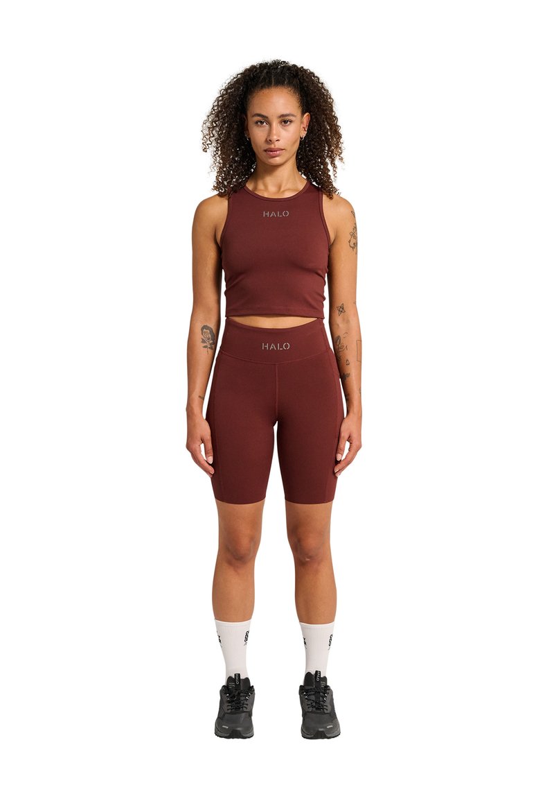 Burgundy sportig crop top och shorts-set med "HALO"-logotyp. Materialet är slätt, passformen är åtsittande. Modellen bär svarta sneakers och vita strumpor.