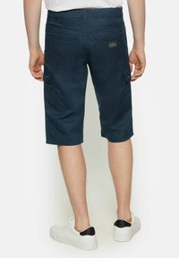 Pantaloni scurți cargo de culoare bleumarin, cu croială dreaptă, două buzunare laterale și o textură netedă, asortați cu adidași albi cu un accent negru la toc.