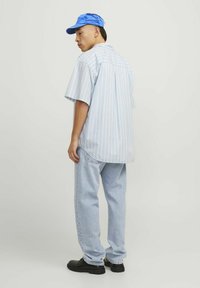 Blauwe button-up shirt met witte verticale strepen, gecombineerd met lichtblauwe jeans en zwarte schoenen, afgemaakt met een blauwe baseballcap.