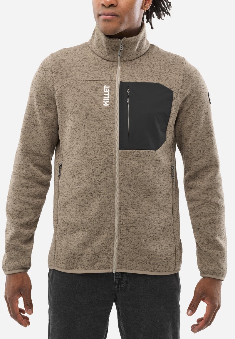 Veste en polaire taupe avec col haut, fermeture éclair intégrale, poche poitrine noire et zippers latéraux. Tissu texturé avec des accents contrastants.