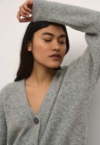 Cardigan grigio chiaro con scollatura a V e motivo a maglia testurizzata, caratterizzato da un singolo bottone scuro sul petto e polsini a costine.