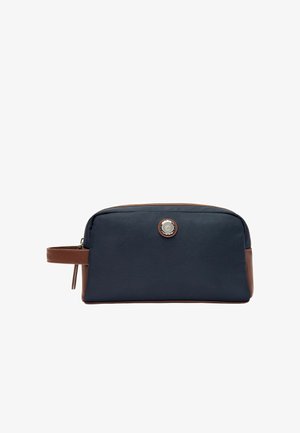 Rechthoekige navyblauwe toilettas met bruine lederen accenten, ritssluiting, zijhandvat en rond metalen logo aan de voorkant in het midden.