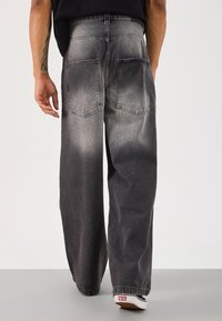 Jeans de mezclilla negra con un ajuste relajado, que cuentan con un lavado descolorido, cinco bolsillos y pierna recta. La tela tiene una textura suave y costuras mínimas.