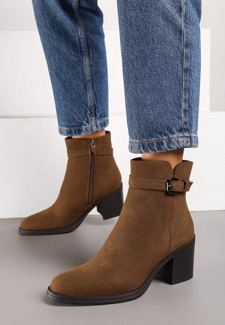 Bottines en suede marron, avec un bout pointu, un talon bloc, une fermeture éclair sur le côté, et une sangle avec une boucle. Portées avec un jean en denim raccourci.