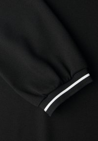 Czarna rękaw bluzy z prążkowanym mankietem ozdobionym białym paskiem, wykonana z miękkiego, teksturowanego materiału.