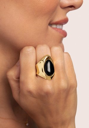 Goldring mit einem polierten schwarzen ovalen Stein, geschwungenes Design mit einer glatten Oberfläche, getragen an einer Hand mit natürlicher Hautstruktur.