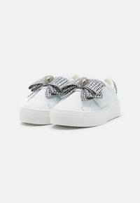Baskets blanches avec une finition en cuir lisse, dotées d'un grand nœud texturé en argent et de pièces décoratives sur les lacets. Semelles en caoutchouc épaisses.