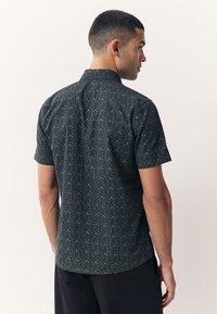 Košulja s kratkim rukavima od tamnog tkanog materijala s cvjetnim motivima. Ovratnik s ležernim krojem, s diskretno teksturiranom površinom.