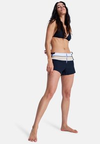 Haut de bikini noir associé à un short foncé avec une ceinture rayée blanche et beige. Le short est muni d'un cordon de serrage réglable.