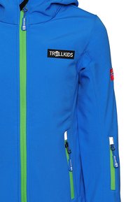 Blue softshell jacket with a green zipper, front logo patch, two side zip pockets, and a hood. Features smooth texture and durable material.