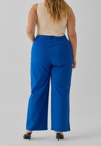 Modré široké kalhoty vyrobené z bavlny, s dvěma zadními kapsami a jednou boční kapsou. Mají hladkou texturu látky a vysoký pas.