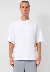 Witte oversized t-shirt van katoen, met een ronde halslijn en korte mouwen. Soepele textuur, rechte zoom, gedragen met grijze shorts.