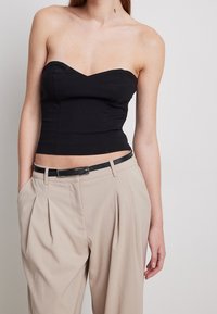 Top nero senza spalline con scollatura a cuore, design aderente, abbinato a pantaloni beige a vita alta con cintura nera.
