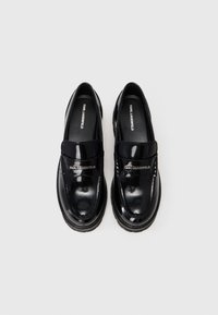 Ein Paar schwarze, glänzende Leder-Lederschuhe mit dicken Sohlen und dem Karl Lagerfeld-Logo oben und auf der Innensohle, von oben gezeigt.