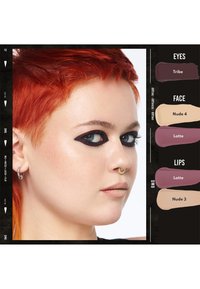 Persona con capelli corti di un rosso brillante, eyeliner nero ad ala audace, rossetto nude sottile, orecchino a cerchio argento e anello al setto d'oro, rivolto a destra.