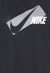 Musta puuvillainen T-paita, jossa on suuri harmaa Nike-swoosh-logo ja rohkea valkoinen "NIKE" -teksti etupuolella. Silkkinen rakenne, rento muotoilu.