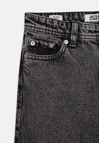 Jeans de denim negro con un corte relajado, con costuras en contraste, herrajes de metal y una textura desgastada en la tela.