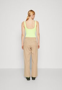 Neon grønn tettsittende tank-top, beige vide bukser og svarte sko med grønne detaljer; enkelt design med glatte teksturer.