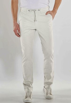 Helle beige Hosen mit einem Kordelzugbund und einem strukturierten Muster. Getragen mit weißen Sneakers, die ein schlankes Design aufweisen.