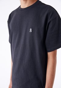 Sort bomulds T-shirt med rund hals, løs pasform og lille broderet globe-logo på venstre bryst. Glat stofstruktur.