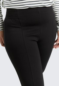 Zwarte leggings met een gladde textuur, voorzien van een hoge tailleband met horizontale ribbels. Ontworpen voor comfort en bewegingsvrijheid.