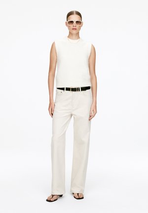 White sleeveless top, cream wide-leg pants, black belt with gold buckle, and black flip-flops. Model wears large white sunglasses.
