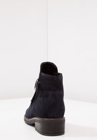 Mörkblå mocka ankelboots med rund tå, kort skafthöjd och tjock klack. Har en dekorativ spänne och minimala sömdetaljer.