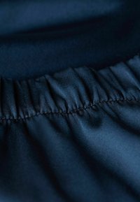 Námořnická modrá látka s hladkým povrchem a nařaseným elastickým detailem podél okraje, vystihující měkký a lesklý vzhled.