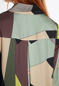 Seidenhemd mit einem abstrakten geometrischen Muster in Grün, Braun, Beige und Schwarz, mit glatter Textur und umgeschlagenem Kragen.
