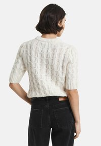 Korte mouwen gebreid trui in crème, met textuurpatronen en een geribbelde hals. Gepaard met hoge taille zwarte jeans.