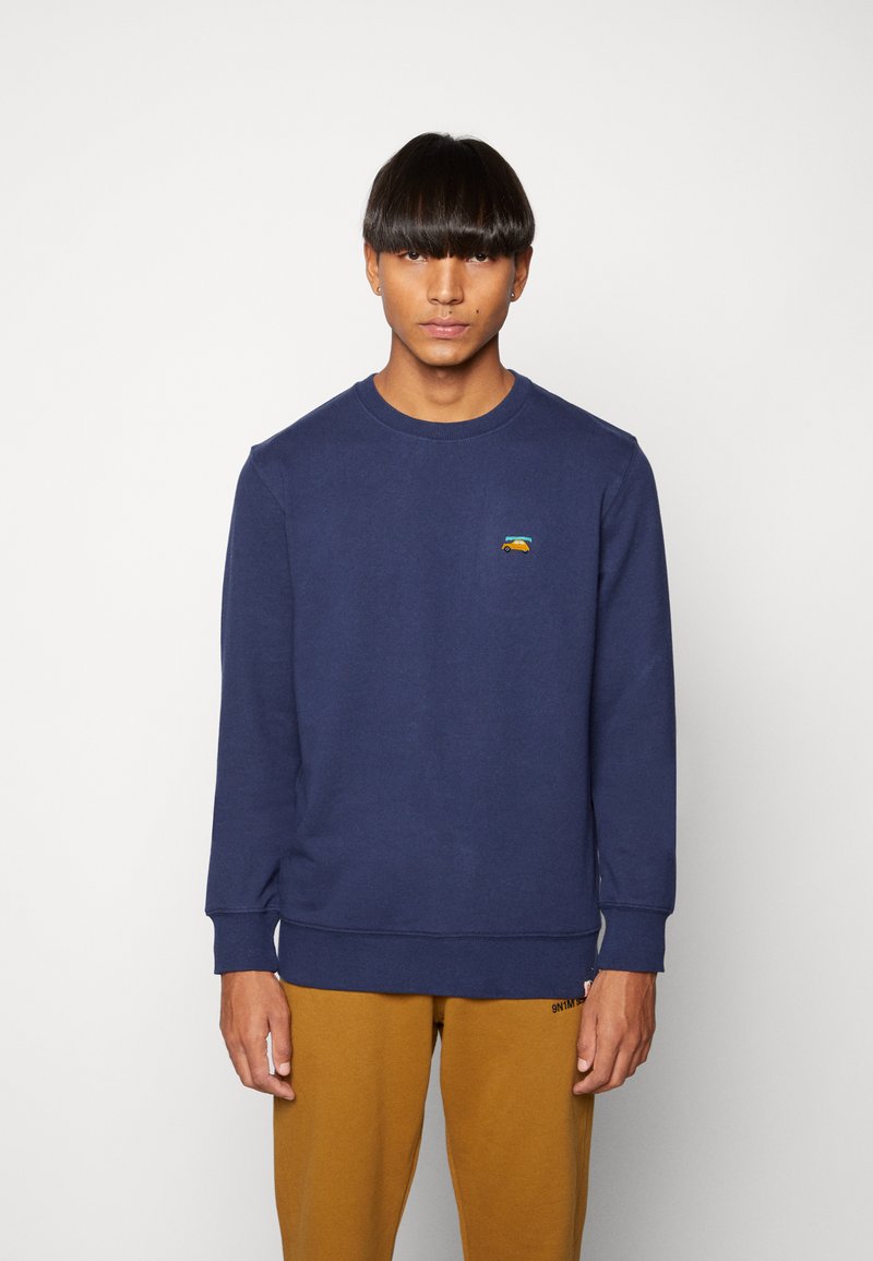 Navy blue sweatshirt with long sleeves and ribbed cuffs, featuring a small colorful logo on the chest. Soft cotton blend material.