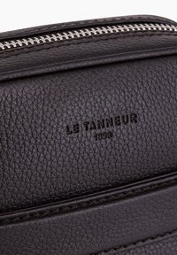 Borsa in pelle marrone con superficie testurizzata, zip argentata e branding impresso. Due sezioni orizzontali distinte visibili.