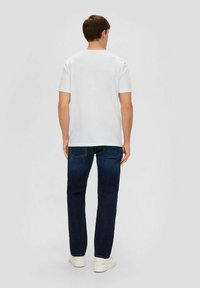 Weißes Baumwoll-T-Shirt mit Rundhalsausschnitt, kombiniert mit dunkelblauen Denim-Jeans. Das Modell steht mit dem Rücken zur Kamera und zeigt die Rückseite des Outfits.