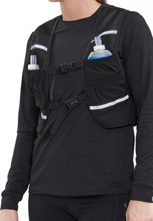 Personne portant un gilet d'hydratation noir avec deux bouteilles d'eau dans les poches avant sur un t-shirt noir à manches longues.