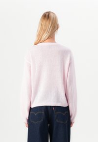 Light pink knit sweater with a loose fit, dropped shoulders, and ribbed hem. The texture appears soft and slightly sheer. Paired with dark jeans.