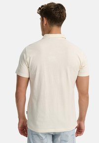 Poloshirt mit kurzen Ärmeln aus cremefarbener Baumwolle, mit einem klassischen Kragen und einem geraden Schnitt. Weiche Textur mit minimalen Details.