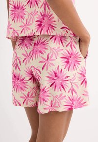 Bermudas con estampado floral en color crema con motivos de flores rosas y un dobladillo en forma de concha. Confeccionadas en tela ligera y con bolsillos laterales.