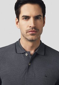 Szary polo z teksturowaną fakturą, z dwoma guzikami i czarnymi detalami na kołnierzyku. Zawiera małe logo po lewej stronie.